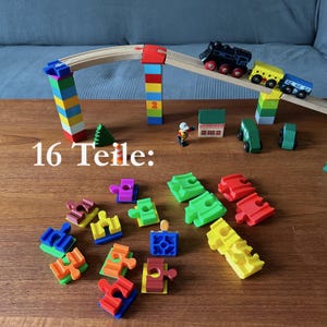 Könnte beinhalten: Ein Holz-Eisenbahnset mit einer schwarzen und gelben Lokomotive, einem gelben und blauen Wagen und einem grünen und gelben Wagen. Das Set enthält auch eine Holzbrücke, zwei Holzpfeiler und ein Holzhaus. Das Set besteht aus 16 Teilen.