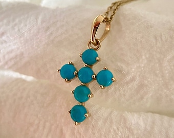 May include: A gold cross pendant with turquoise stones. The cross is made of metal and has a simple design. The turquoise stones are round and have a bright blue color.