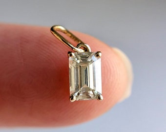 May include: A gold pendant featuring a clear emerald-cut gemstone.