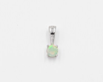 Puede incluir: Un colgante de plata con una piedra preciosa de ópalo redonda. El ópalo tiene una base blanca lechosa con destellos verdes y amarillos. El colgante tiene un diseño simple y elegante, ideal para el uso diario.