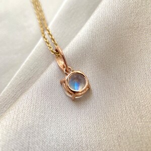 May include: A delicate gold necklace with a round moonstone pendant. The pendant is set in a bezel setting and has a subtle shimmer.