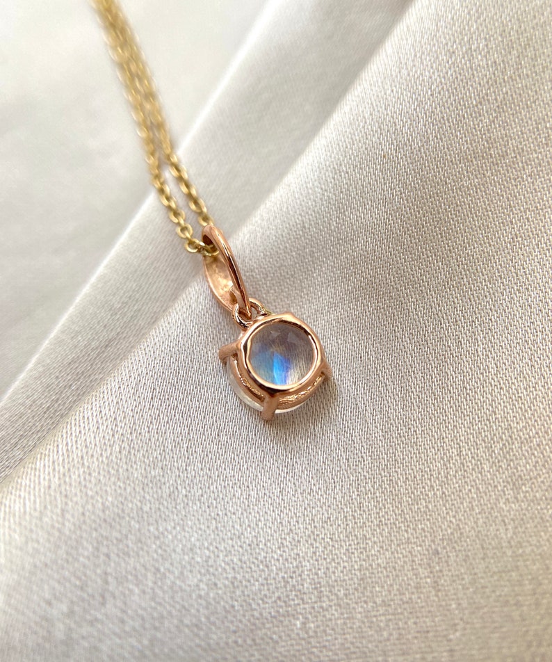 May include: A delicate gold necklace with a round moonstone pendant. The pendant is set in a bezel setting and has a subtle shimmer.