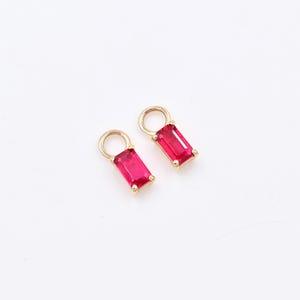 May include: Two gold charms with a small loop at the top and a rectangular red gemstone.