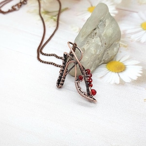Peut inclure: Un collier en fil de cuivre avec un pendentif de forme géométrique orné de perles rouges.