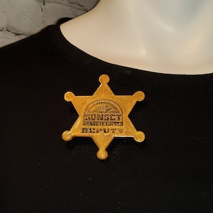 May include: A gold sheriff's star badge with the text "Sunset Ranch" and "Deputy" on it.