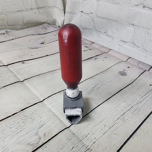 May include: A red and gray toggle switch with a rounded handle. The switch is on a white wooden surface.