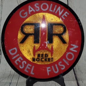 May include: A round, red and black sign with the words "Gasoline Diesel Fusion" around the edge. In the center is a gold circle with the letters "RR" in black and a red rocket ship with the words "Red Rocket" below it.