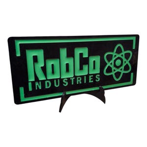 May include: A black sign featuring the text "RobCo INDUSTRIES" in green, accompanied by a green atom symbol. The sign is supported by a black stand.