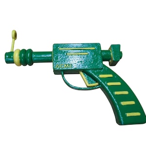 May include: A green toy gun with a yellow trigger and a yellow ring on the barrel. The gun has the word "ACME" printed on the side.