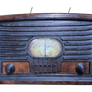 Puede incluir: Radio de estilo vintage con marco de madera oscura y rejilla de altavoz gris oscuro. La radio presenta un dial amarillento con una aguja e indicadores de estación. Dos perillas y una serie de botones son visibles en la sección inferior.