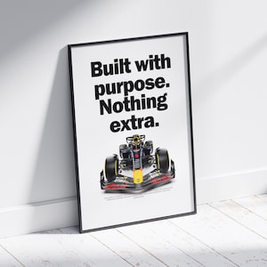 May include: Framed poster featuring a Formula 1 race car. The poster has the text "Built with purpose. Nothing extra." in bold black letters. The race car is red, yellow, and black.