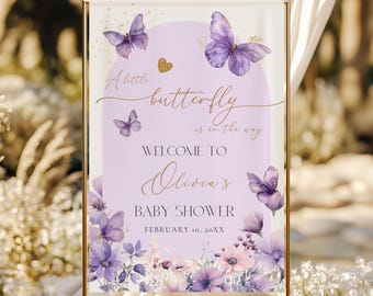 May include: A rectangular welcome sign featuring a light purple arch, gold butterflies, and floral accents. The text reads: A little butterfly is on the way, WELCOME TO Olivia's BABY SHOWER, FEBRUARY 10, 20XX. The design includes purple flowers.