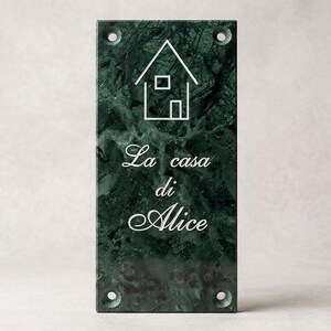 Può includere: Una targa rettangolare in marmo verde scuro con un'icona a linee bianche di una casa nella parte superiore e il testo inciso in bianco "La casa di Alice" centrato sotto. La targa presenta quattro fori di montaggio circolari agli angoli.