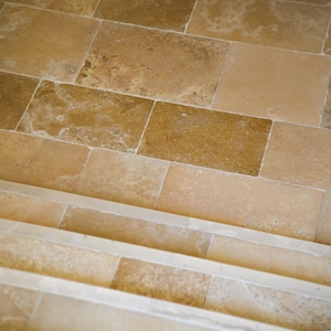 Könnte beinhalten: Nahaufnahme einer Steintreppe mit rechteckigen Fliesen in Beige- und Brauntönen. Die Stufen bestehen aus demselben Stein und erzeugen ein zusammenhängendes und natürliches Aussehen. Die Fliesen haben eine strukturierte Oberfläche.