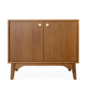 Può includere: Un mobile in legno con due ante e pomelli in ottone. Il mobile è realizzato in legno marrone chiaro e ha un design moderno della metà del secolo. Poggia su quattro gambe angolate.