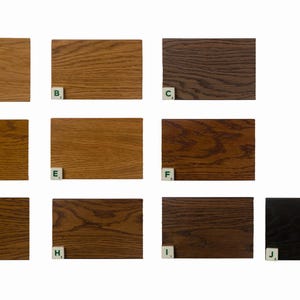 May include: A collection of ten wooden samples, each a different shade of brown, ranging from light oak to a deep ebony. Each sample is a rectangular shape, with visible wood grain patterns. Small letter tiles are placed at the bottom of each sample.