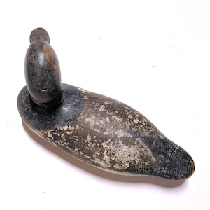 May include: A vintage duck decoy, painted in shades of gray, brown, and black. The wooden decoy features a detailed head and body, with a weathered appearance. The duck's head is turned, and the body is elongated.