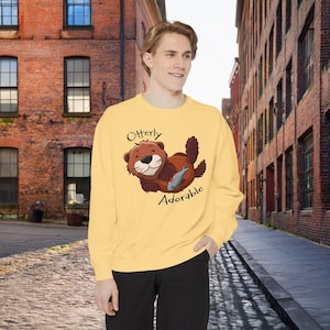 May include: A yellow sweatshirt with a cartoon otter holding a fish and the text "Otterly Adorable".