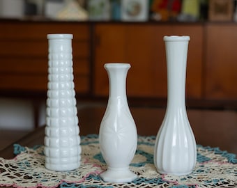 May include: Three white ceramic vases of different shapes and sizes. The vase on the left has a textured, raised pattern. The vase in the center has a star-shaped design. The vase on the right has a fluted design.