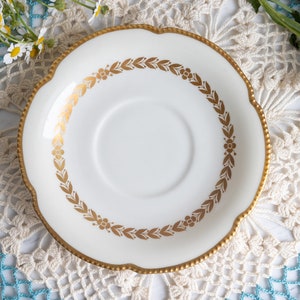 May include: White saucer with a gold rim and a gold floral design around the edge.
