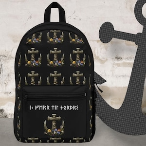 Puede incluir: Mochila negra con un patrón repetido de un diseño de martillo de piedra con flores. El bolsillo frontal presenta el mismo diseño de martillo y texto blanco. Tiene un asa superior y correas ajustables.