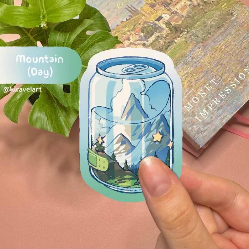 Op de afbeelding: Een blauwe en groene sticker van een blikje met een berglandschap erin. Het blikje heeft een pleister erop en sterren aan de hemel. De tekst "Mountain (Day)" en "@kiravelart" staan op de sticker.