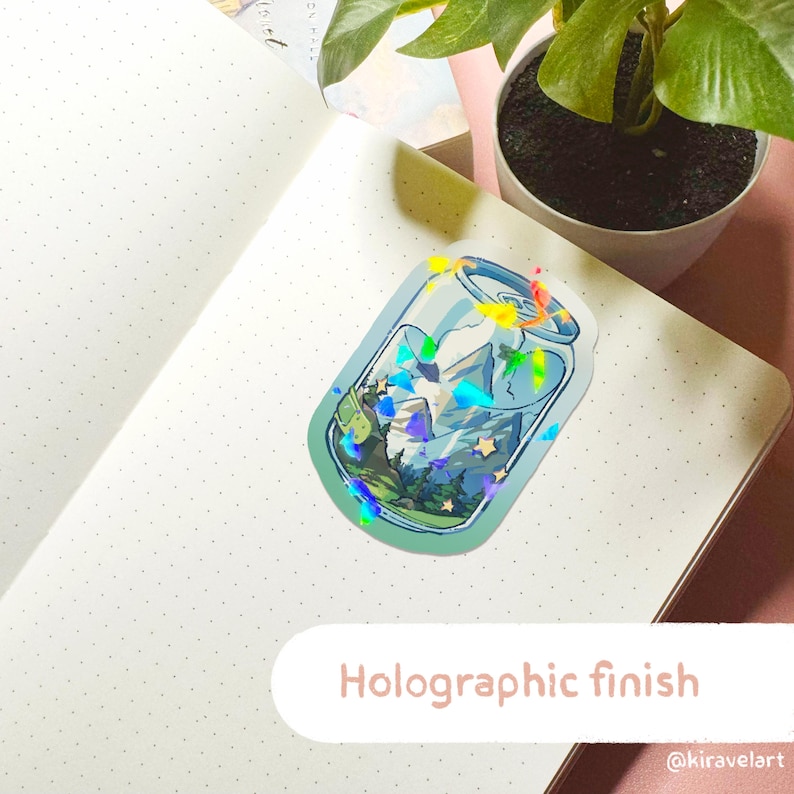 Op de afbeelding: Een holografische sticker van een blikje met een berglandschap erin. Het blikje is blauw en groen met een witte rand. Het berglandschap is een blauw en groen landschap met witte sterren. De sticker heeft een holografische afwerking die in het licht glinstert.