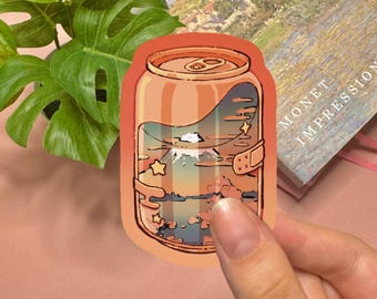 May include: A die-cut sticker shaped like an orange soda can featuring a landscape illustration inside. The design depicts a mountain peak, clouds, and stars in a sunset color palette. The sticker has a smooth, rounded edge and a glossy finish.