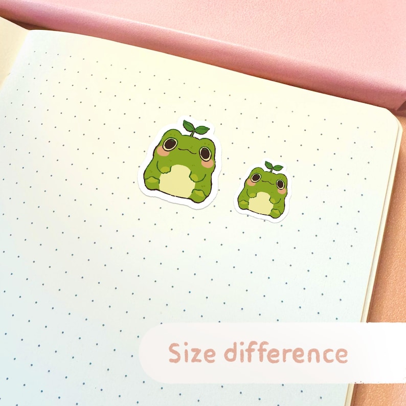 May include: Two green frog stickers with a small plant on their heads. The stickers are on a white dotted background. The text "Size difference" is written on a pink rectangle at the bottom of the image.