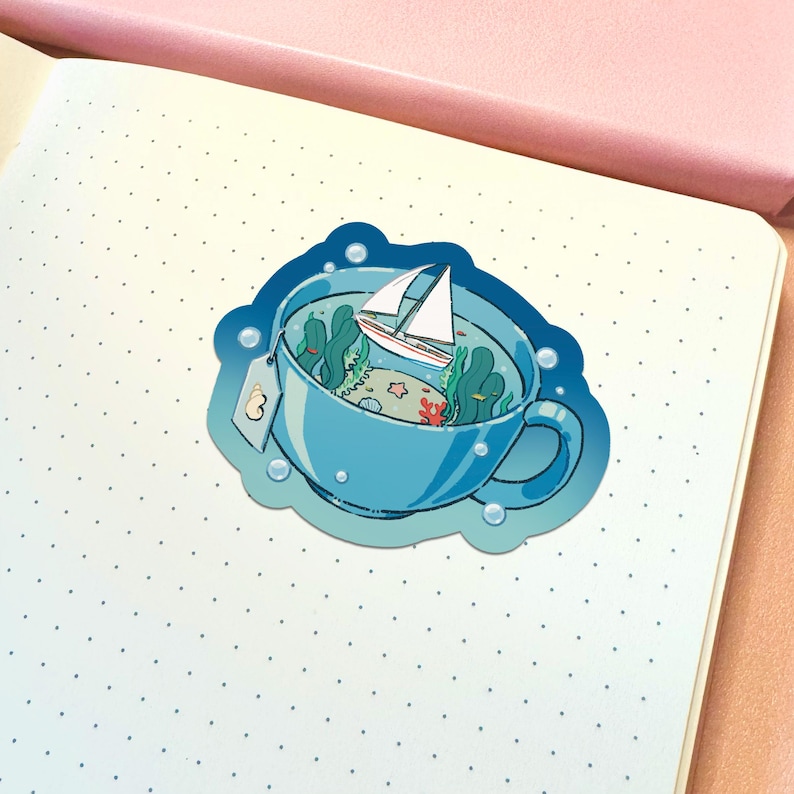 May include: A die-cut sticker featuring a light blue teacup filled with ocean water, green seaweed, a small white sailboat, a starfish, and a seashell. A tea bag tag with a shell illustration hangs from the side of the cup, surrounded by bubbles.