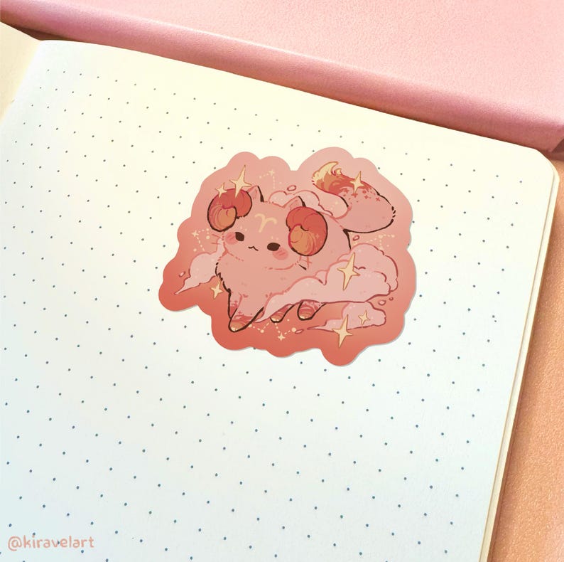 May include: A pink and orange sticker featuring a cartoon cat with ram horns, surrounded by clouds and stars. The cat is wearing a pink and orange outfit and has a cute expression on its face.