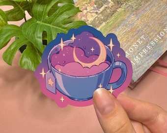 May include: A die-cut sticker featuring a blue teacup filled with swirling purple and pink clouds and a crescent moon. The design includes a tea bag tag with a star icon and several four-pointed star accents surrounding the cup in a vibrant color palette.