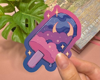 May include: A die-cut sticker shaped like a popsicle with a purple wooden stick. The top portion features a dark blue night sky with a crescent moon, stars, and constellations, transitioning into pink clouds and a melting pink base with sparkles.