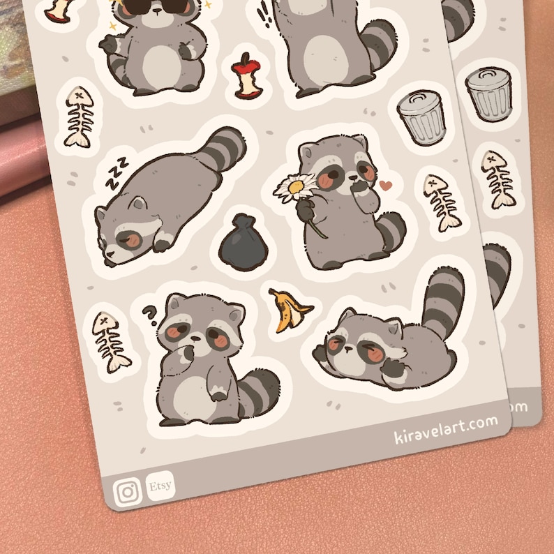 May include: A sticker sheet featuring various cartoon raccoon illustrations in shades of gray, brown, and black. The designs include raccoons sleeping, holding a daisy, and wearing sunglasses, alongside small icons like fish bones, trash cans, and fruit cores.