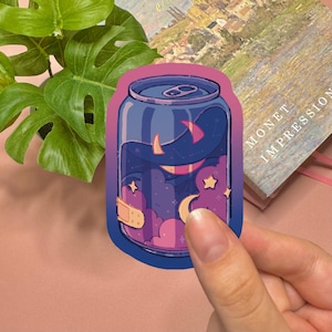 May include: A die-cut sticker shaped like a soda can featuring a night sky scene with purple clouds, yellow stars, and a crescent moon. The can has a gradient blue and pink border and a small beige adhesive bandage graphic on the lower left side.