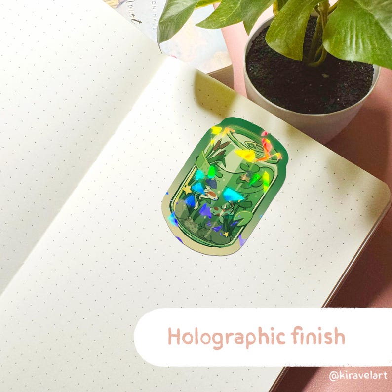 May include: A green sticker with a holographic finish, featuring a jar design with aquatic plants and fish. The sticker is placed on a dotted notebook page. Text at the bottom reads "Holographic finish".