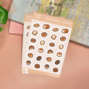 Op de afbeelding: Een lichtbruin stickervel met de titel Mini Bakery en de code BMSS002, met diverse kleine illustraties van bakproducten zoals broden, croissants, bagels en muffins gerangschikt in een rasterpatroon op een lichte achtergrond.