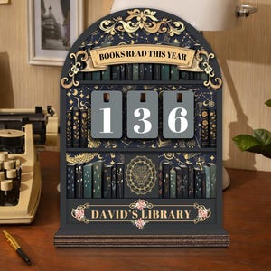 May include: A dark blue wooden bookshelf-shaped counter with the text "BOOKS READ THIS YEAR" and "DAVID'S LIBRARY". The counter displays the number "136". The bookshelf is decorated with gold accents and illustrations of books.