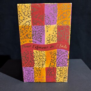 Könnte beinhalten: Rechteckige Parfümbox mit farbenfrohem Patchwork-Design. Die Box zeigt Quadrate in Rot, Lila, Orange und Gelb mit einem floralen Muster. Der Text "Pour l'Amour de l'Inde" ist auf einem roten Banner zu sehen.