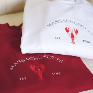 May include: Two sweatshirts, one white and one red, with an embroidered lobster and the text "MASSACHUSETTS EST. 1788".