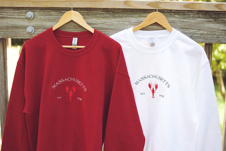 May include: Two long-sleeved sweatshirts with a red lobster and the text "MASSACHUSETTS EST. 1788" embroidered on the front. One sweatshirt is red and the other is white.
