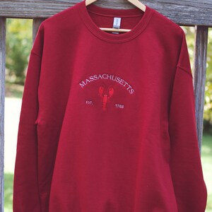 May include: Red sweatshirt with a white embroidered design that says "MASSACHUSETTS EST. 1788" with a lobster in the center.