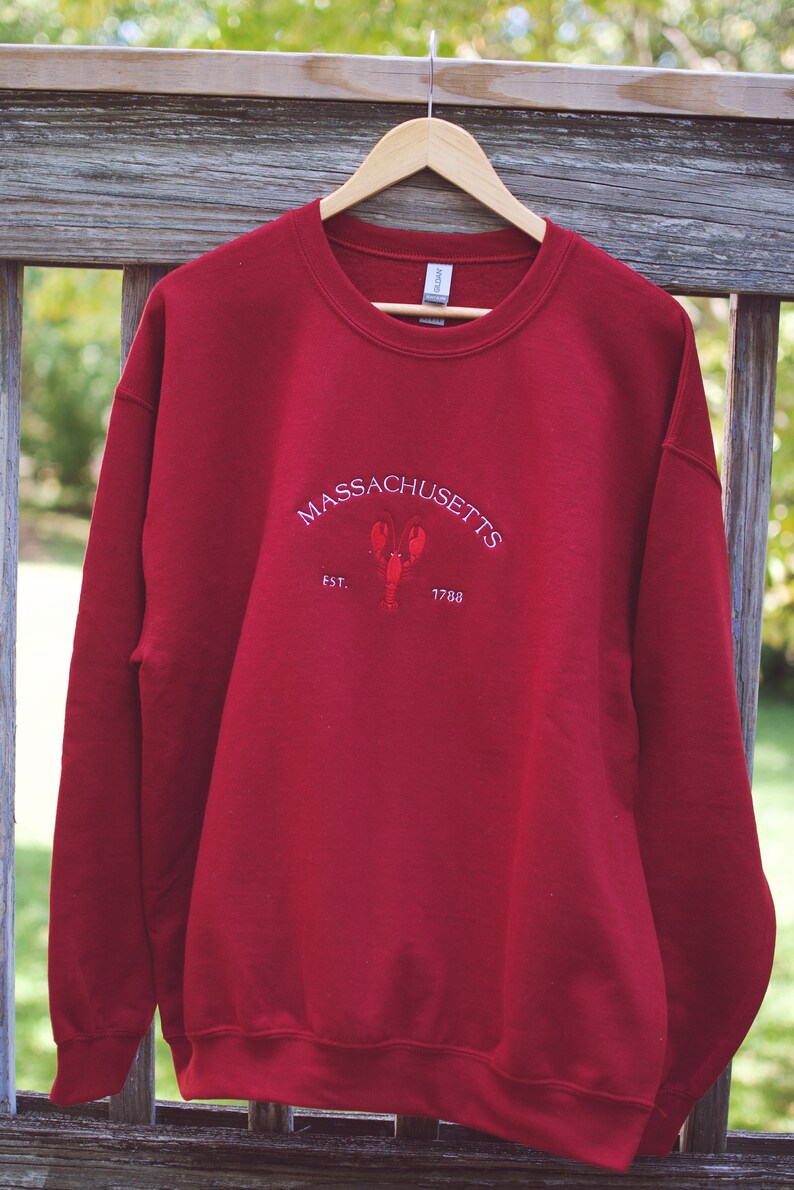 May include: Red sweatshirt with a white embroidered design that says "MASSACHUSETTS EST. 1788" with a lobster in the center.