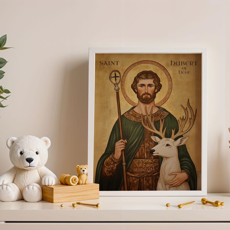 May include: A framed print featuring Saint Hubert of Li&egrave;ge, depicted with a deer. The artwork has a gold background and is framed in white. The text "SAINT HUBERT OF LIEGE" is visible. A white teddy bear and other decorative items are in the foreground.