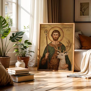 May include: A framed artwork featuring Saint Hubert of Li&egrave;ge, holding a staff and embracing a white deer. The artwork has a gold background and is in a wooden frame. The text "Saint Hubert of Liege" is visible.