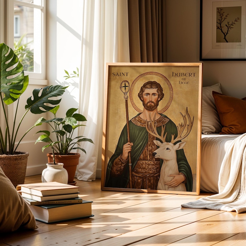 May include: A framed artwork featuring Saint Hubert of Li&egrave;ge, holding a staff and embracing a white deer. The artwork has a gold background and is in a wooden frame. The text "Saint Hubert of Liege" is visible.