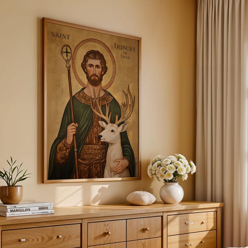 May include: A framed artwork featuring a religious figure holding a staff and a white deer. The artwork has text that reads "SAINT" and "HUBERT OF LIEGE". The artwork is displayed above a wooden dresser with a plant, books, and a vase of flowers.