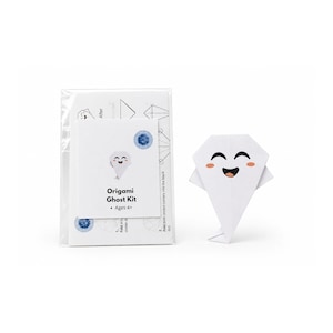 Può includere: Un kit per fantasma in origami in una busta di plastica trasparente con istruzioni e una figura di fantasma in carta bianca con un volto sorridente, occhi neri, una bocca larga e guance rosa. La confezione riporta il testo Origami Ghost Kit.