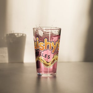 May include: A clear glass with a pink liquid inside. The glass has a graphic of a snake and the text "uishy's Reptiles" printed on it.
