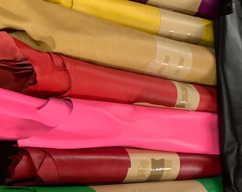 May include: A stack of rolled leather hides in various colors, including purple, yellow, tan, red, pink, green, white, and brown. The hides are wrapped in brown paper and secured with tape.